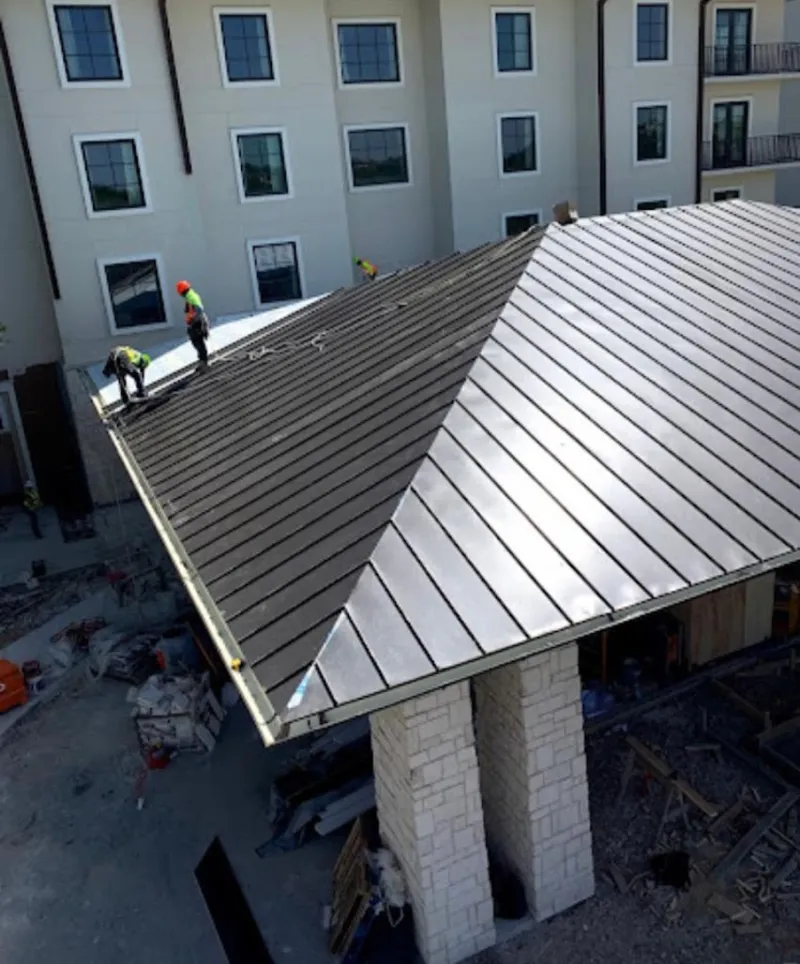 Crew installing standing seam metal roof panels on a commercial project in Alton